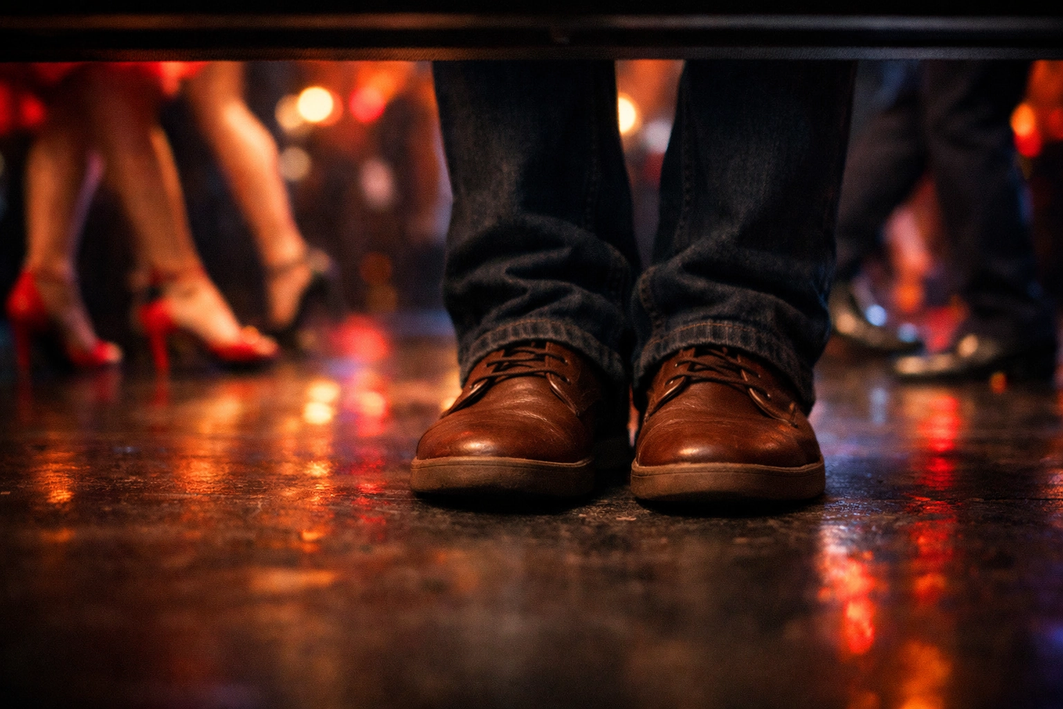 Pies inmóviles bajo mesa de discoteca en primer plano, mientras pies de bailarines se mueven al fondo, representando el miedo a bailar salsa